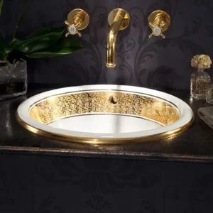 lavabo in oro e ceramica bianca in un bagno con carta da parati scura e floreale. Rubinetteria a parete oro